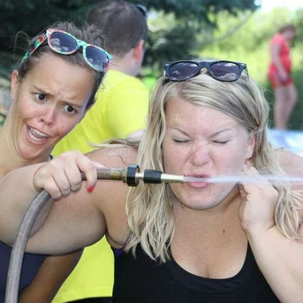 Zwei komische Frauen trinken aus Gartenschlauch im Fruehling